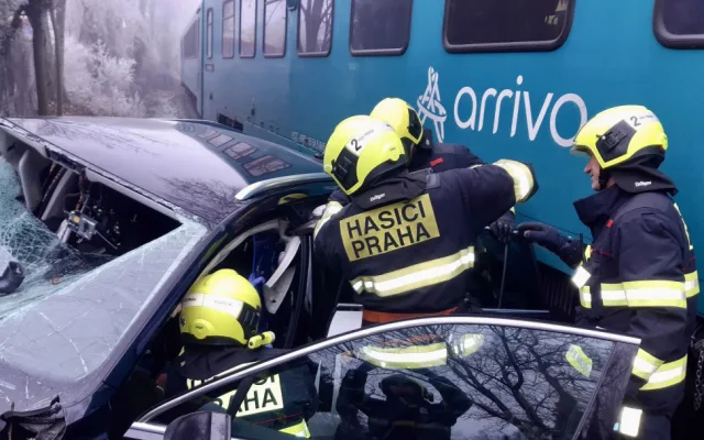 Vlak na přejezdu v Praze smetl auto, řidiče museli hasiči vystříhat