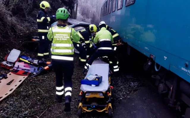 Vlak na přejezdu v Praze smetl auto, řidiče museli hasiči vystříhat